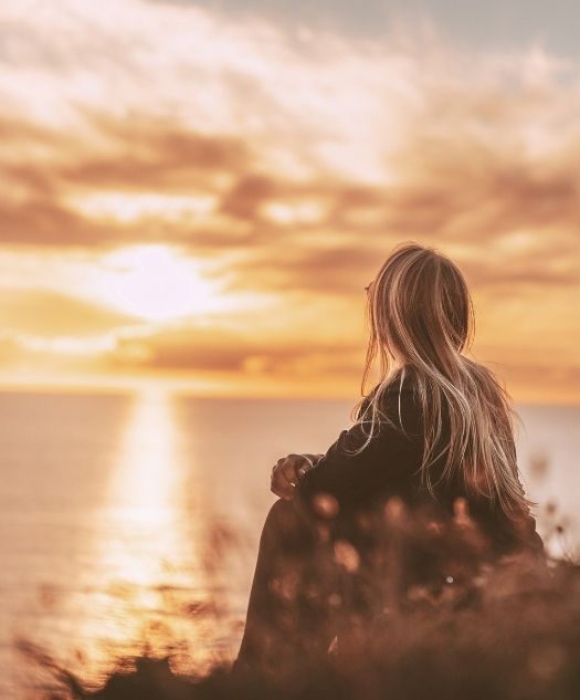 Counseling services in Sint Maarten. woman sitting on a hillside with amber colored flowers staring across the ocean at a golden sunset